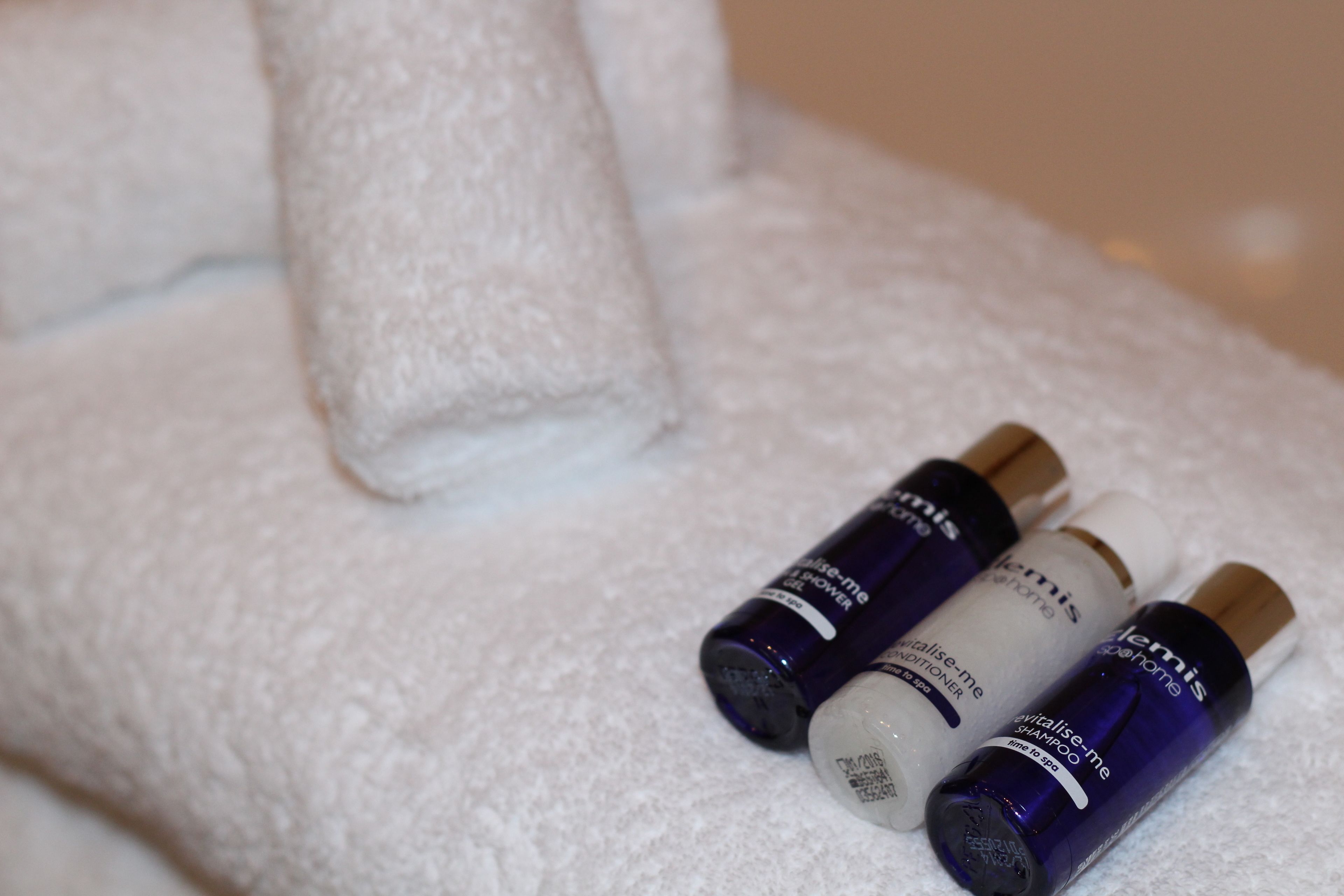 A white towel and three bottles of hair care products on a white surface.