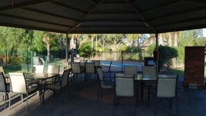 A covered patio area with tables and chairs, a pool, and a fenced garden. - Sportslander Motor Inn (Moama)
