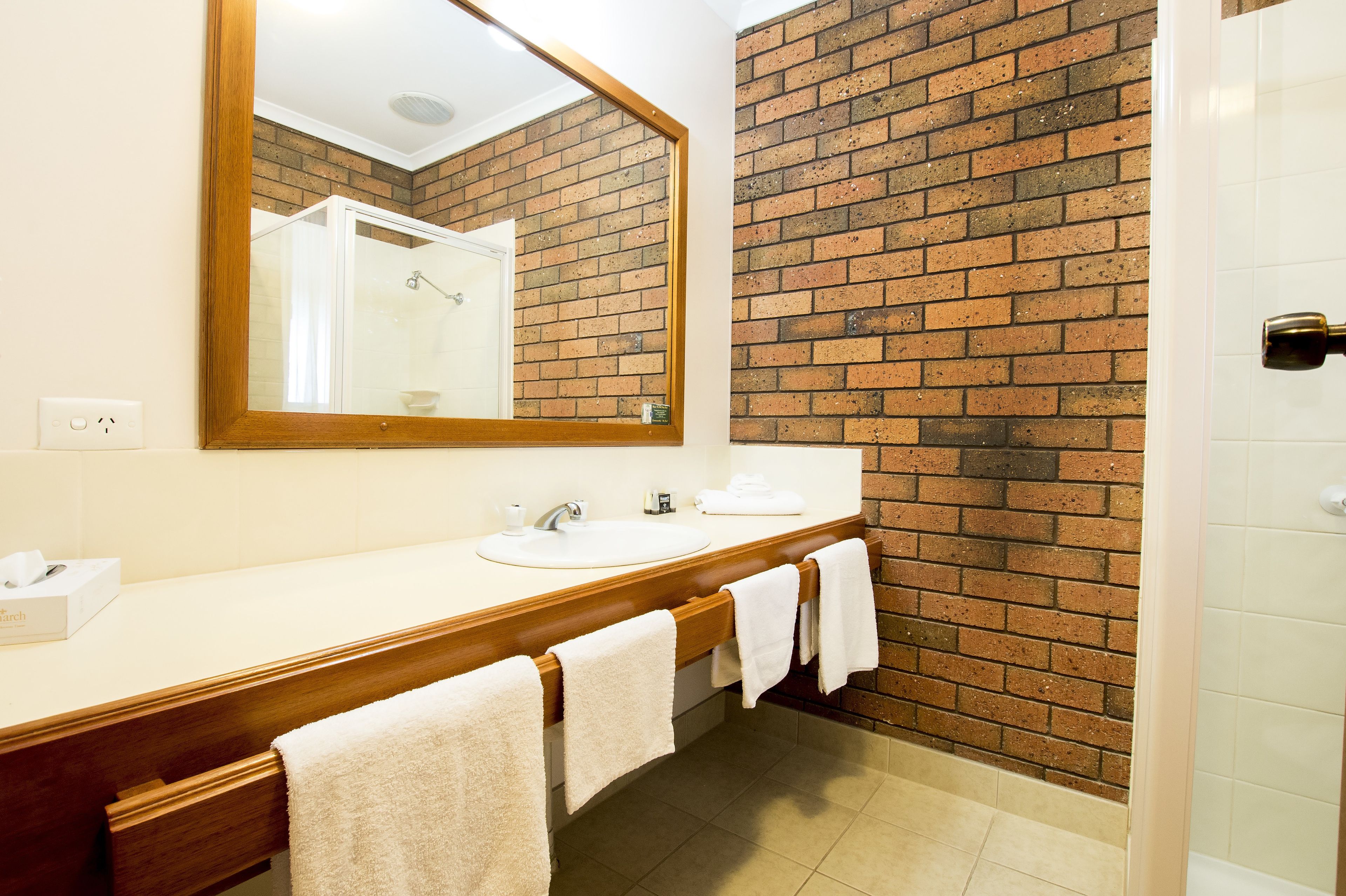 A bathroom with a wooden vanity, a large mirror, a sink, and a shower area.