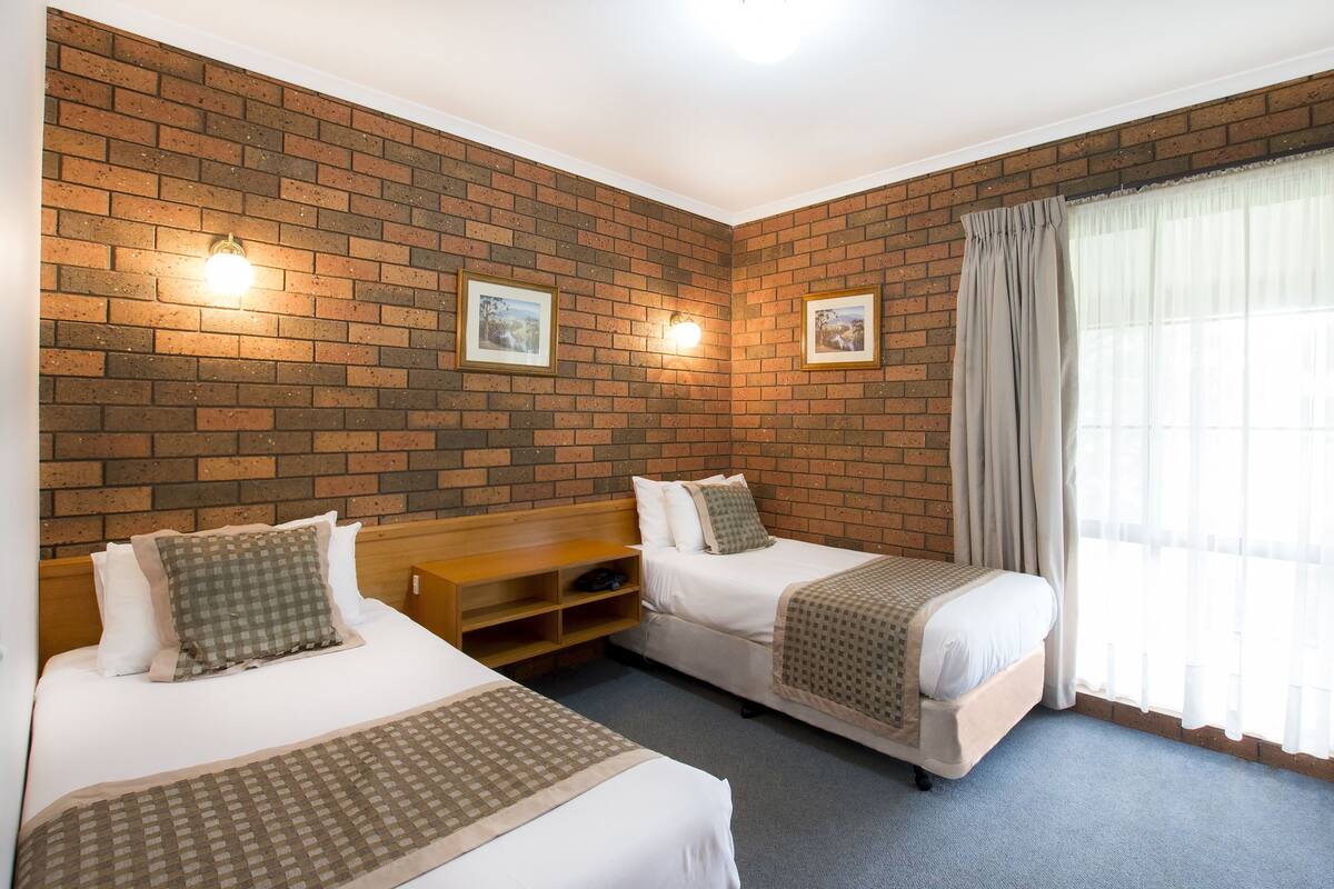 A room with two beds, a brick wall, and a window with curtains.