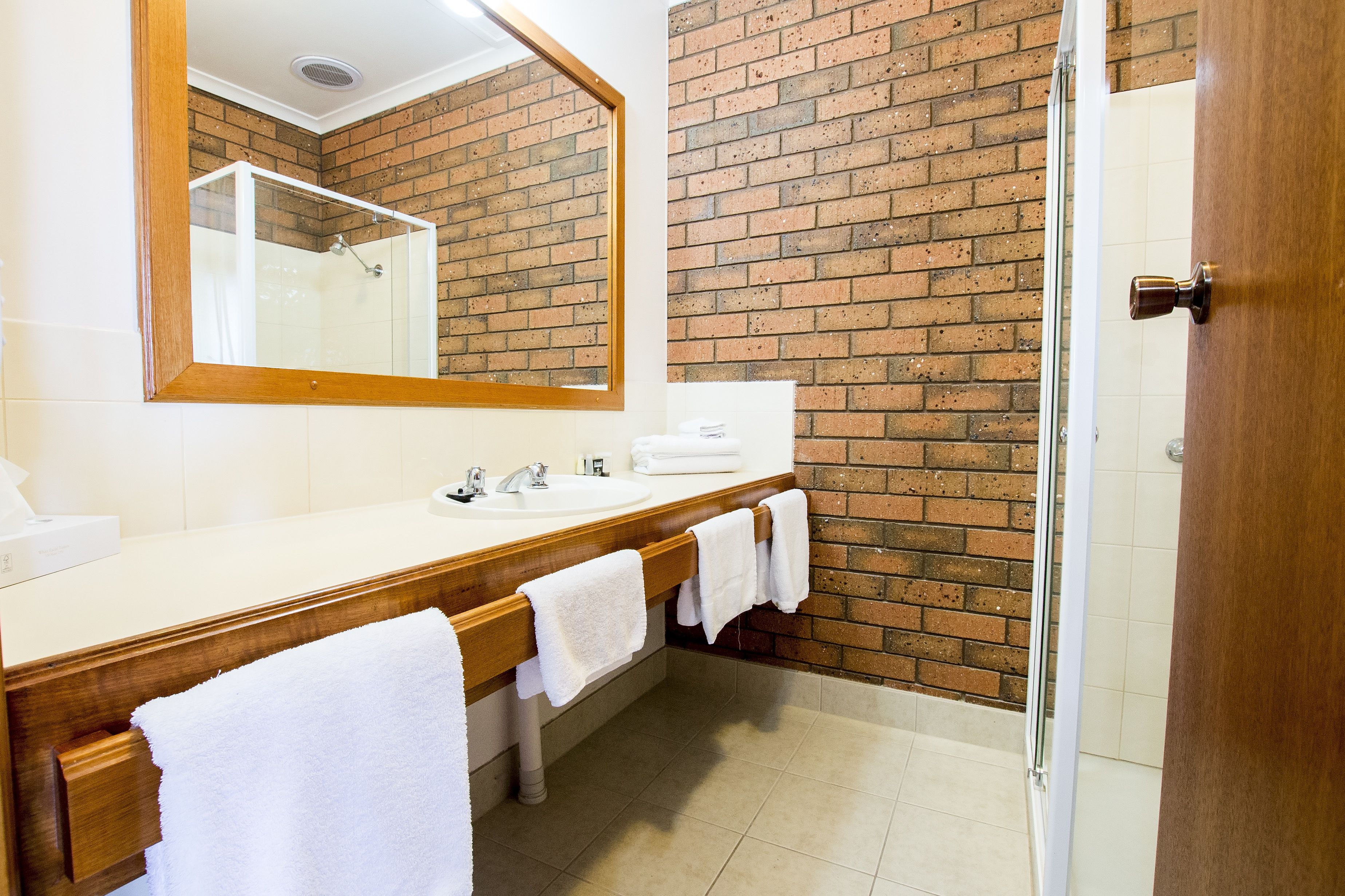 Un baño con tocador de madera, dos lavamanos, un espejo y una pared de ladrillo.