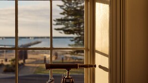 A telescope on a tripod in a window with a view of a body of water and a tree. - The Customs House Port MacDonnell (Port Macdonnell)