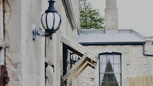 A narrow brick pathway leading to a building with a chimney, a window with curtains, and a black lantern on the wall. - The Customs House Port MacDonnell (Port Macdonnell)