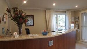 Una recepción con un florero, certificados enmarcados en la pared y una ventana con cortinas.