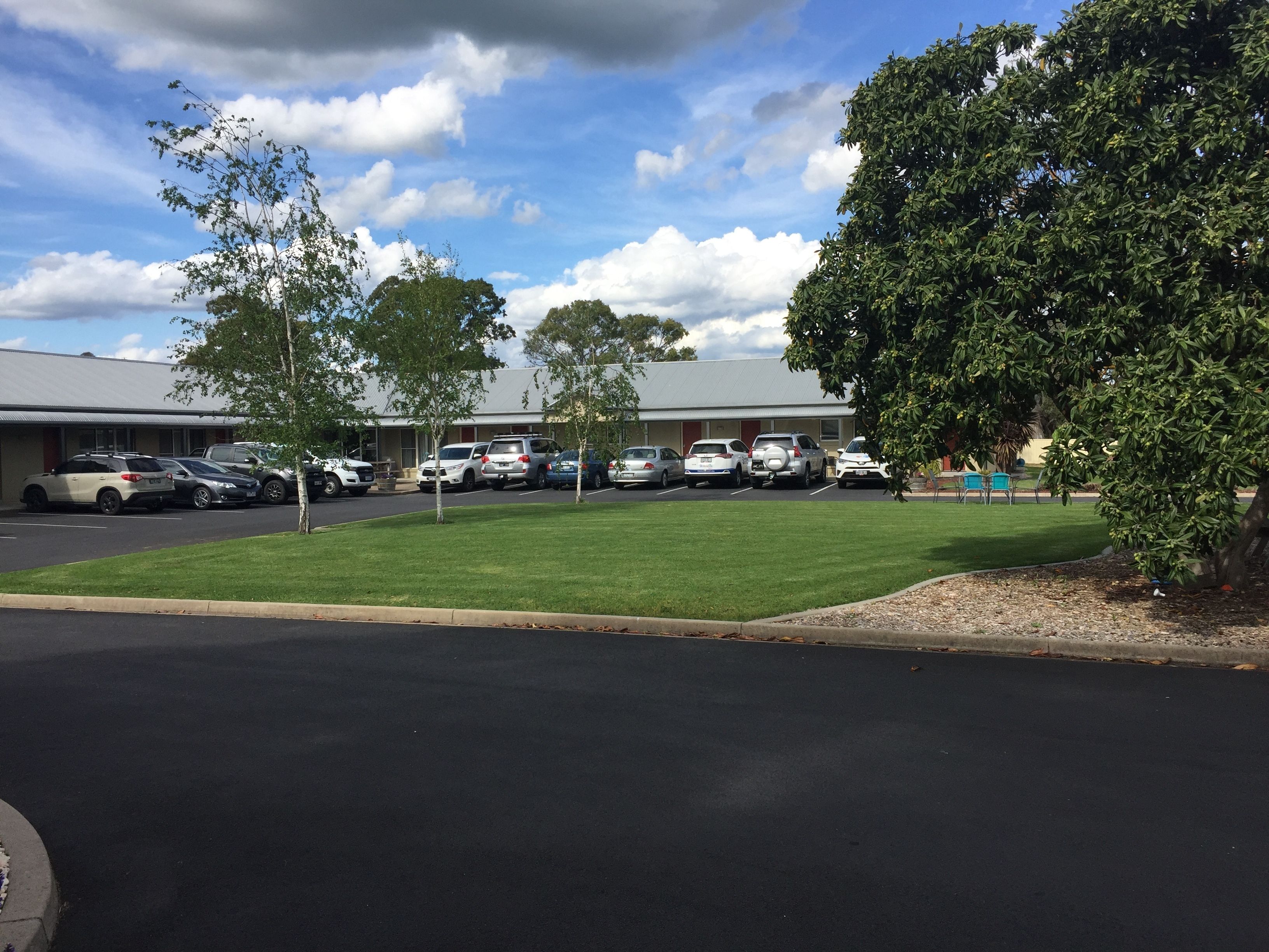 A parking lot with several cars parked in front of a building with a flat roof and a small lawn area.