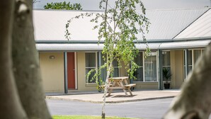 Un motel con una construcción de un solo nivel, una zona de estacionamiento techada y un pequeño espacio exterior para sentarse.
