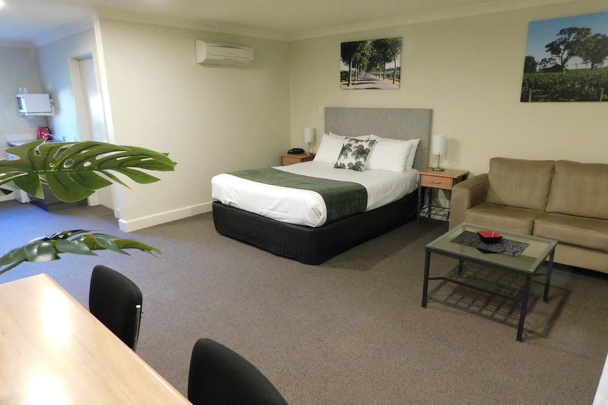 Una habitación de hotel con una cama, un sofá, una mesa de centro y una planta grande.