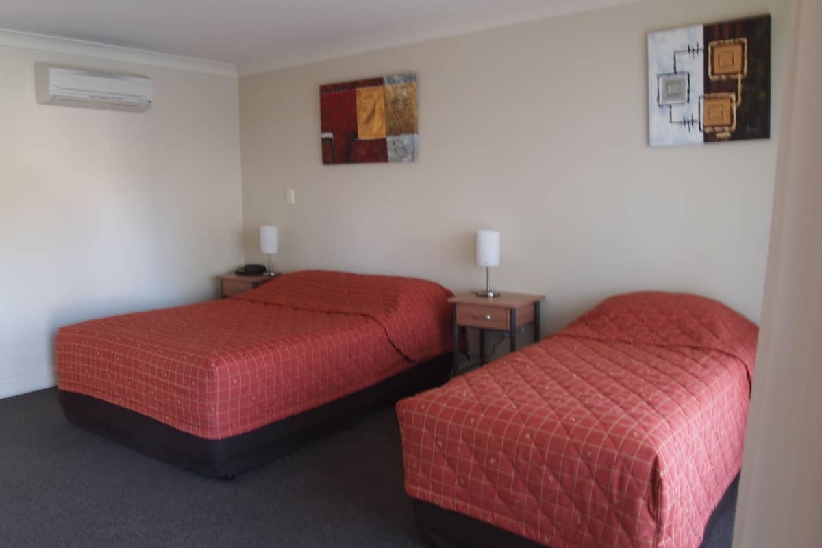 Una habitación de hotel con dos camas individuales, una mesita de noche con lámpara y un aire acondicionado de pared.
