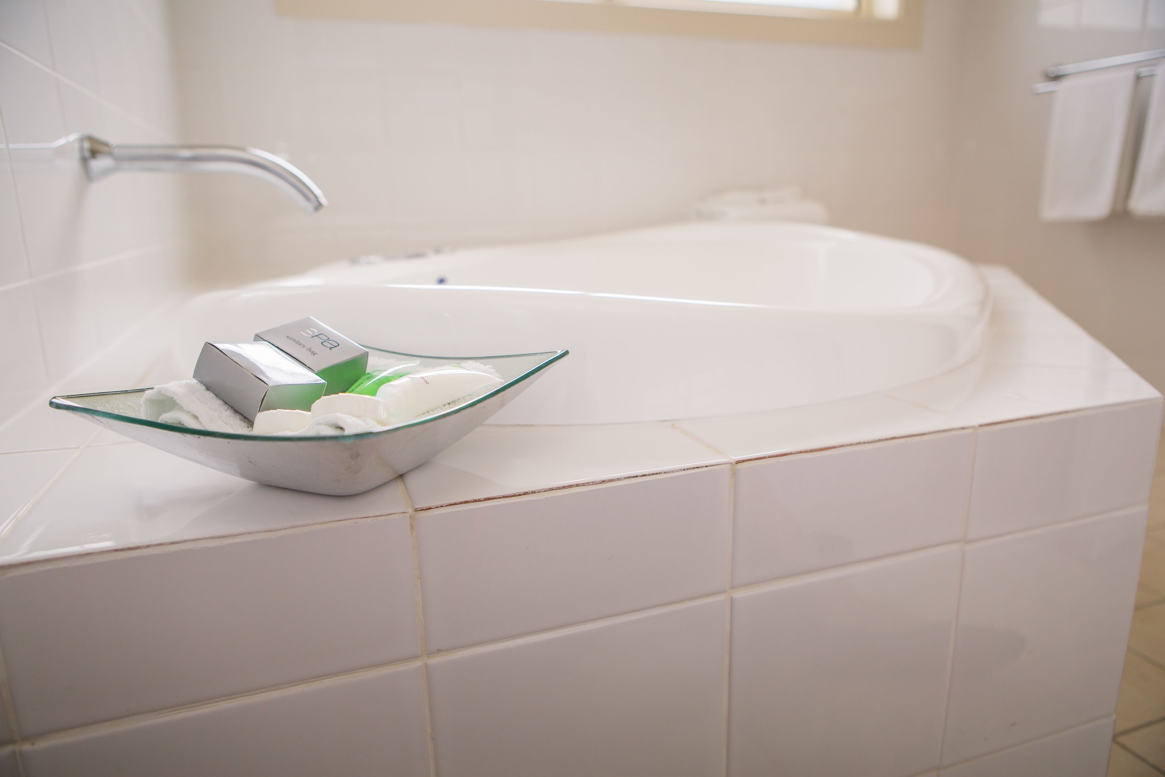 A bathroom with a glass bowl containing toiletries, a white bathtub, and a chrome faucet.