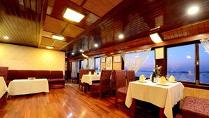 A restaurant with wooden flooring, tables set with white tablecloths, and chairs. - Imperial Classic Cruise Halong (Tuan Chau)