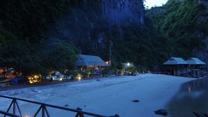 A beach resort with thatched-roof huts, a wooden deck, and a calm sea. - Imperial Classic Cruise Halong (Tuan Chau)