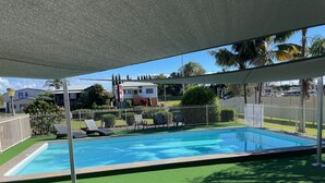 A swimming pool with a covered area, surrounded by a white fence and green artificial turf. - City Centre Motel (Kempsey)