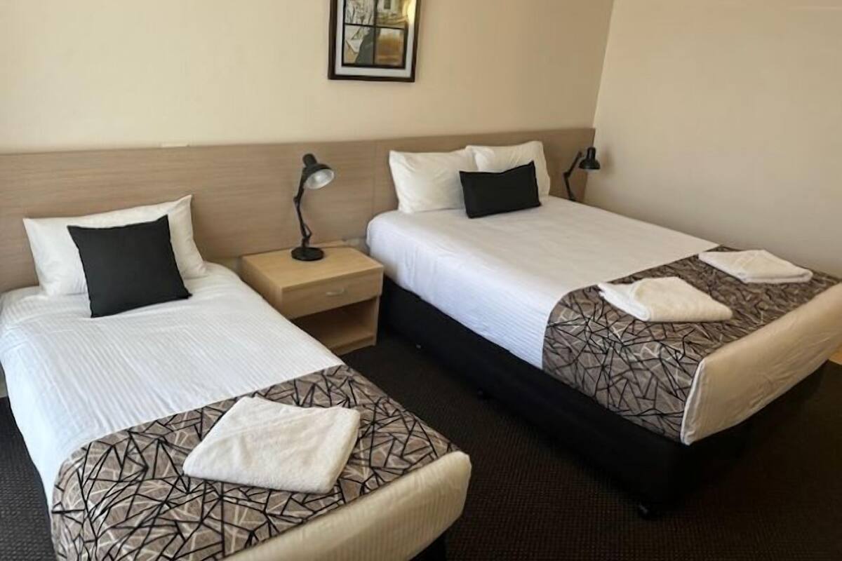 A hotel room with two beds, a nightstand with a lamp, and a framed picture on the wall.