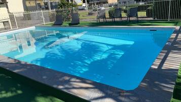 Una piscina con una valla blanca, sillas de descanso y un edificio con un letrero al fondo.