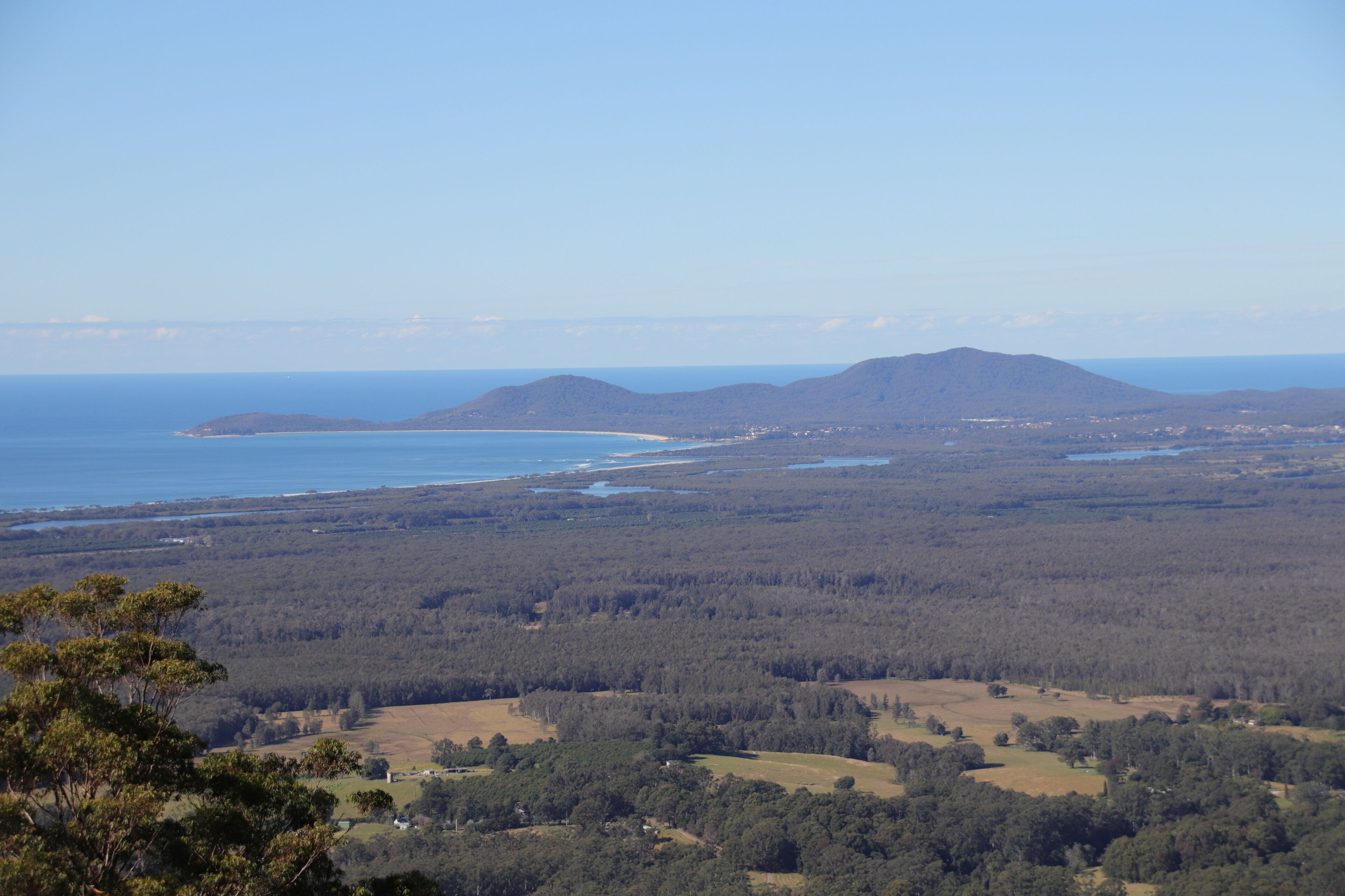 A coastal landscape with a view of the sea, hills, and forested areas.