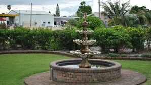 A circular brick fountain with a statue in the center, surrounded by a well-maintained lawn and various plants. - City Centre Motel (Kempsey)