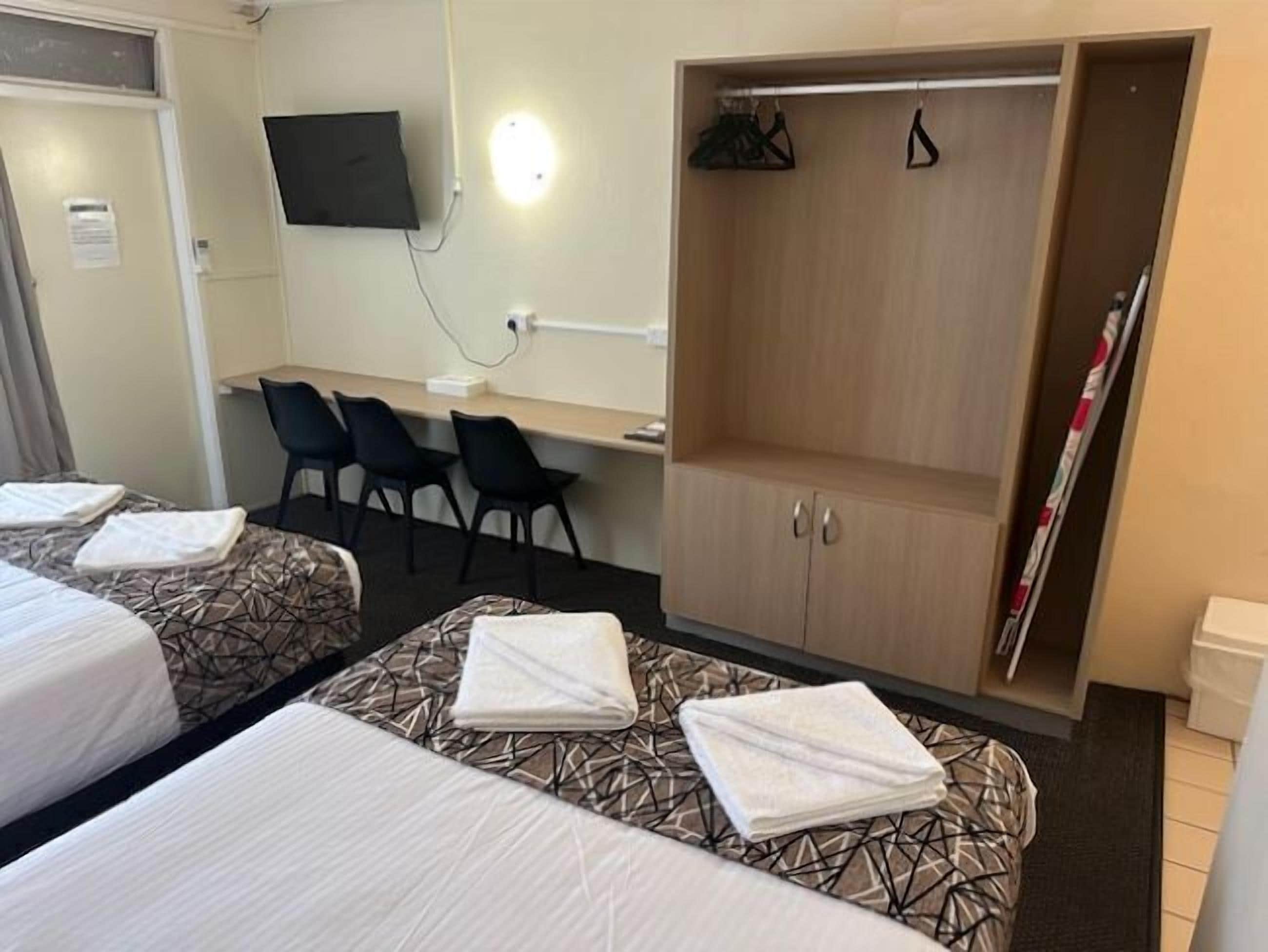 A hotel room with two beds, a desk, a TV, and a wardrobe.
