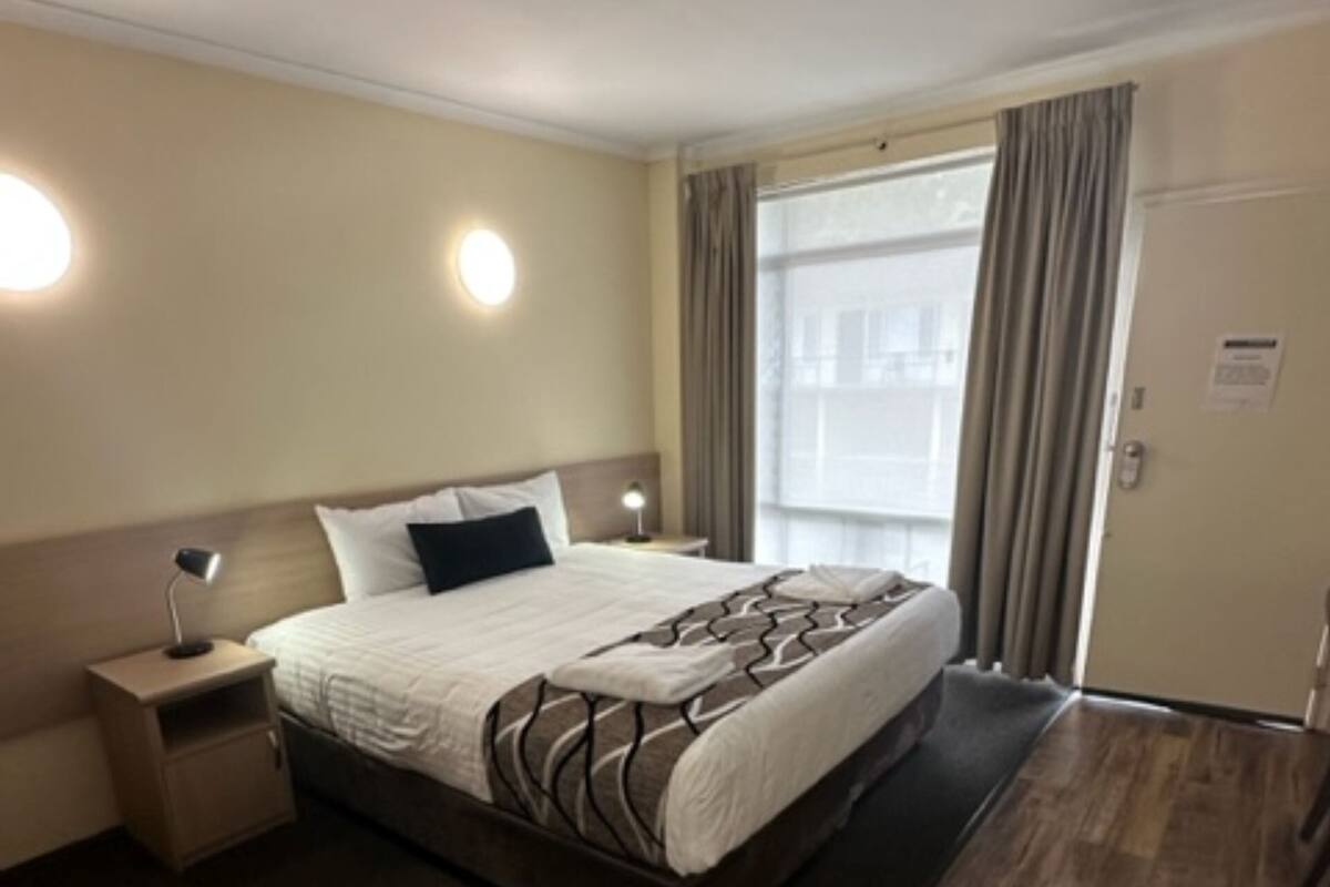 A hotel room with a large bed, a nightstand, a lamp, a window with curtains, and a door.