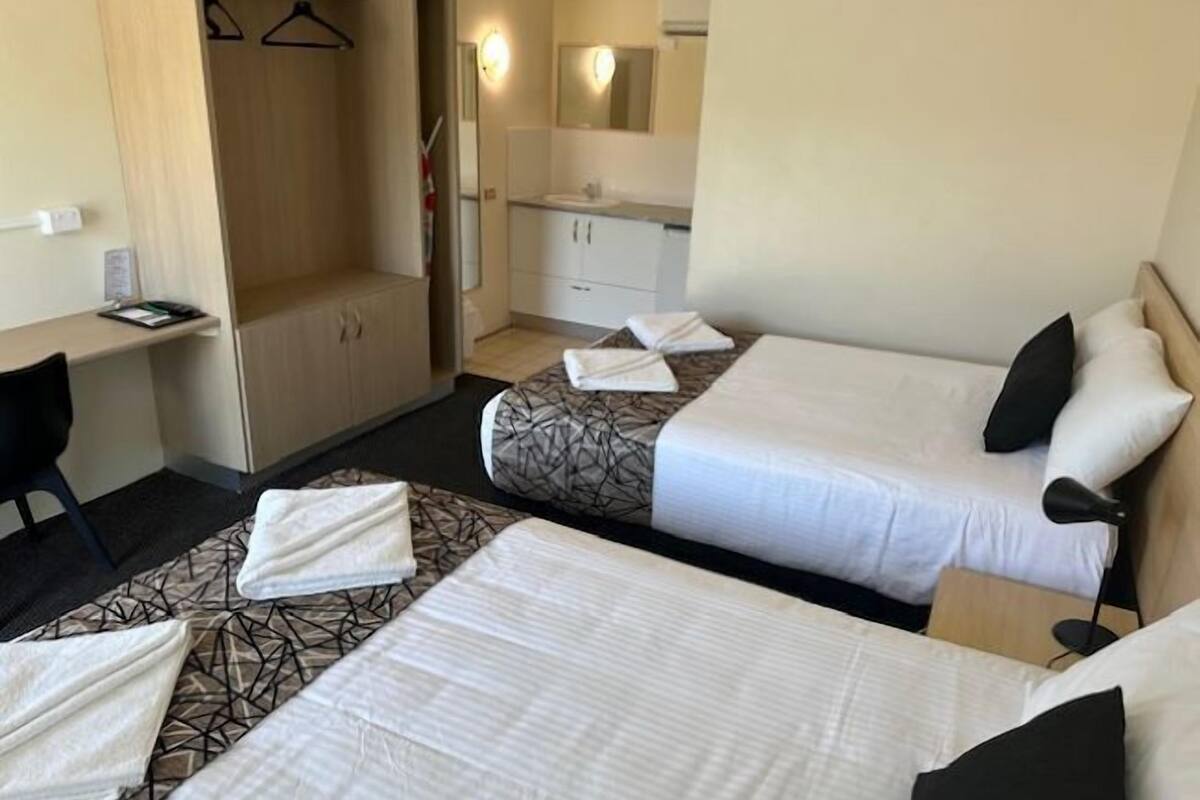 A hotel room with two beds, a desk, a wardrobe, and a bathroom.