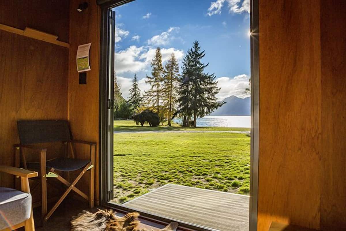 Una habitación con un amplio ventanal que ofrece vistas a un área verde, árboles y una masa de agua.