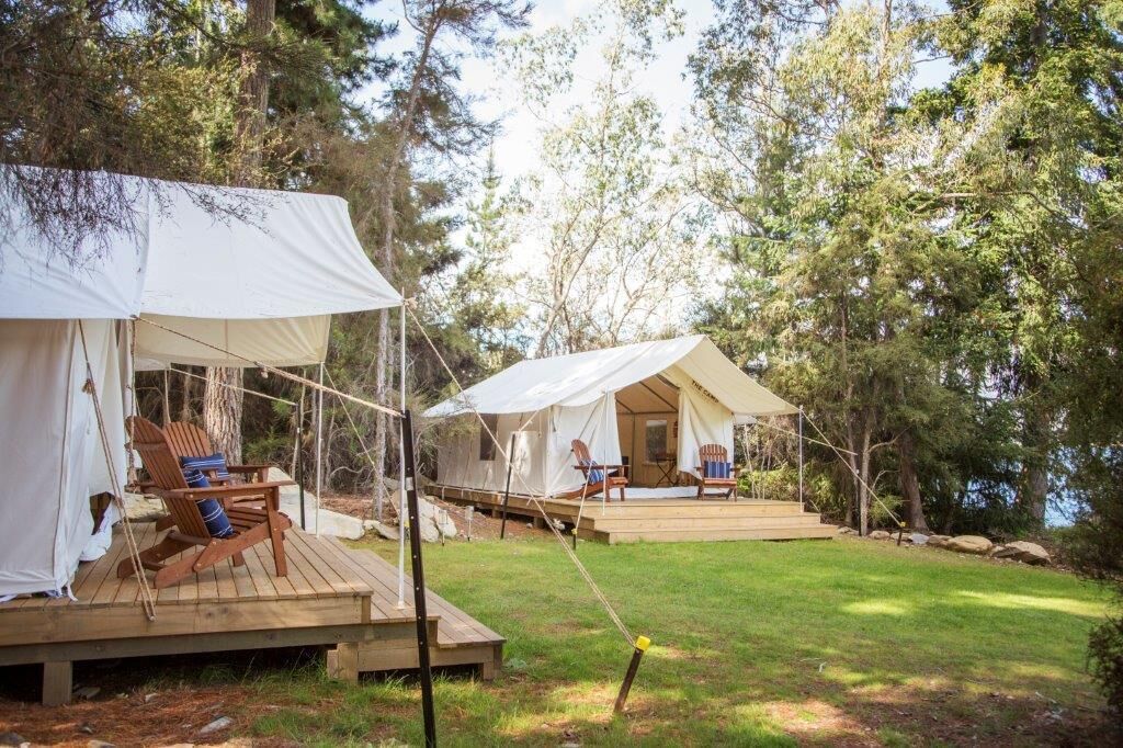 Deux tentes dotées de terrasses en bois, chacune comprenant une chaise et une table.