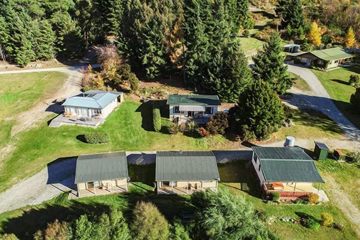 Vista aérea de una zona residencial con tres casas, cada una con un estilo de techo diferente, rodeadas de un bosque frondoso y un césped bien cuidado.