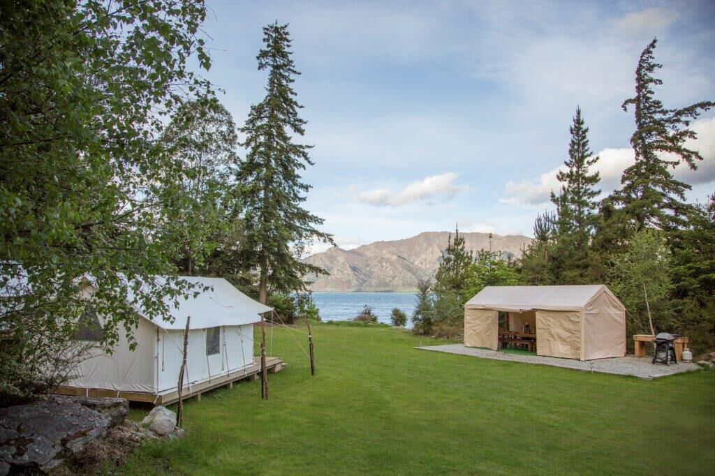 A campsite with two tents, a grassy area, and a lake with mountains in the background.