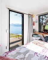 Quarto com cama, escrivaninha, cadeira, janela com vista para um lago e montanhas, e um extintor de incêndio na parede.
