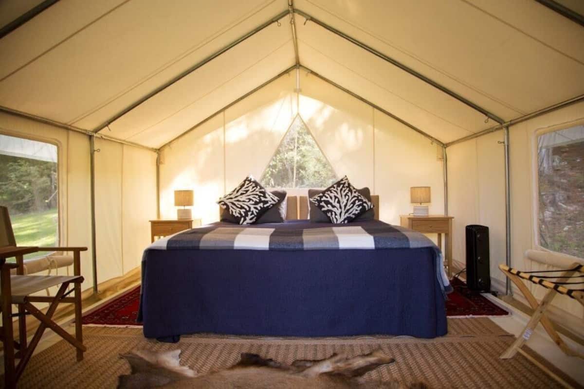 Una habitación con carpa, una cama, dos mesitas de noche, una silla y vistas al exterior.