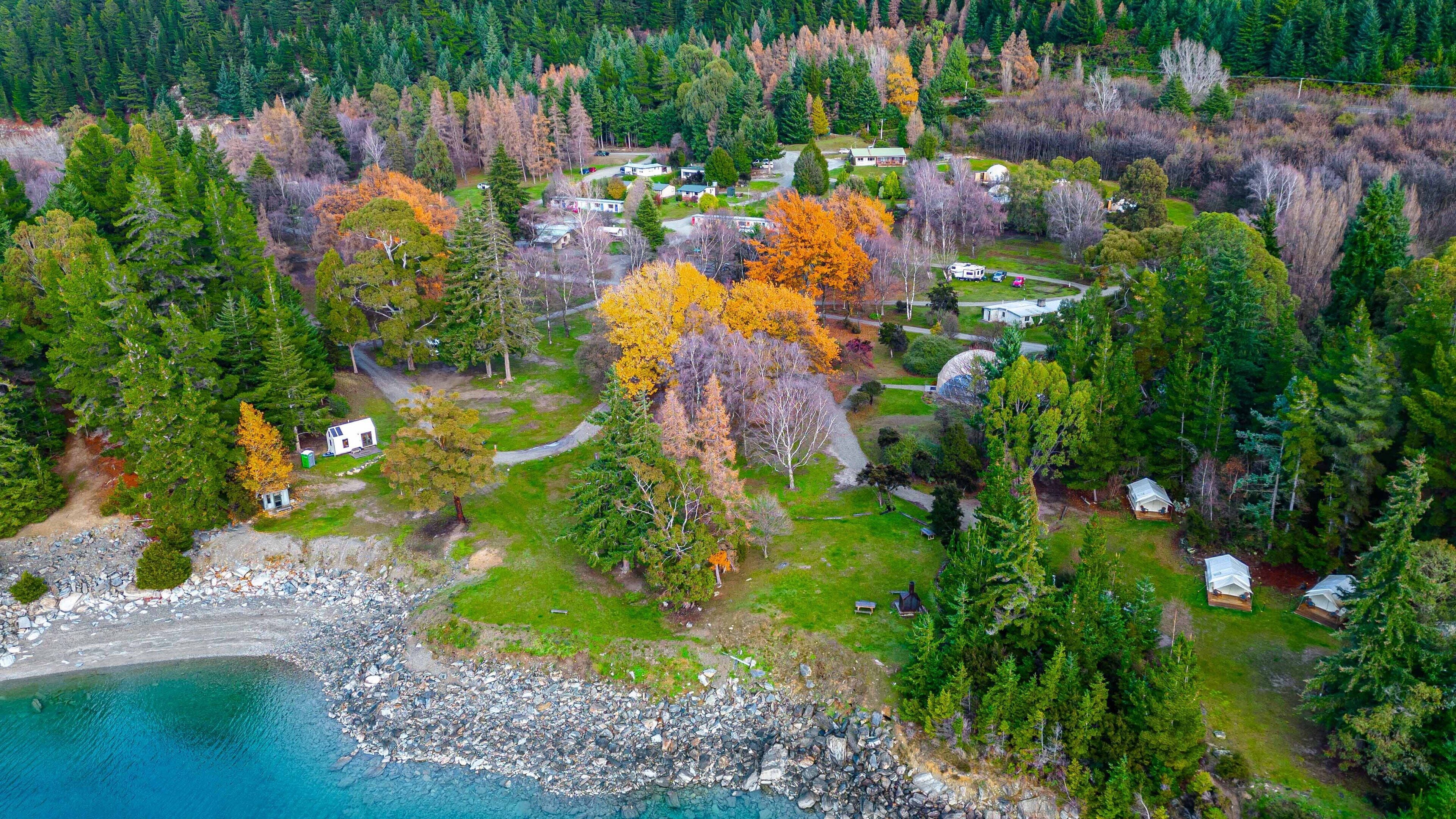 Vista aérea de un camping con vehículos recreativos, cabañas y una zona de playa.