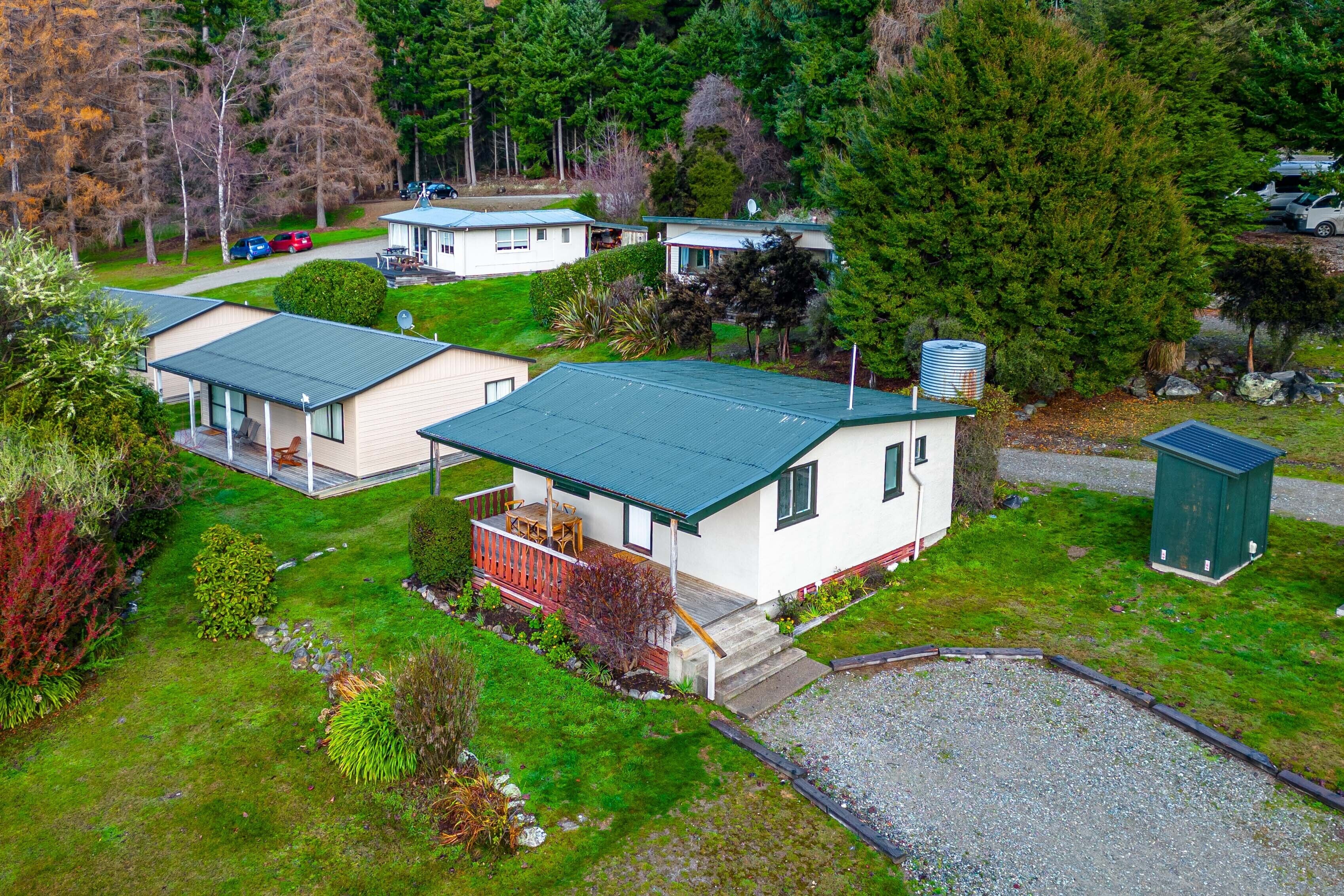A residential area with two single-story houses, each with a green roof, surrounded by lush greenery and trees.