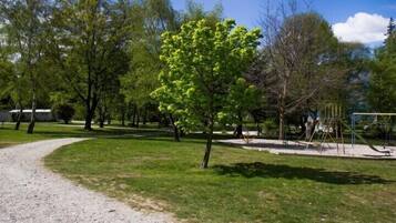 Stroll through the park's well-maintained grassy area along a gravel path, surrounded by trees and a family-friendly playground.