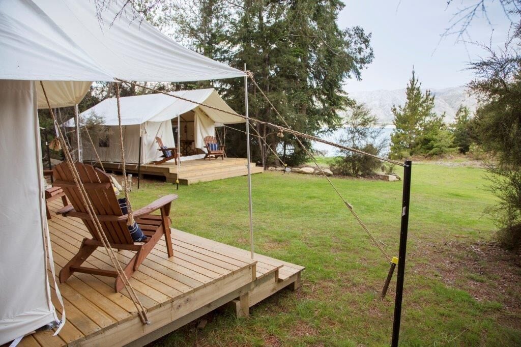 Alojamiento en tienda de campaña con terraza de madera, asientos al aire libre y vistas del paisaje circundante.