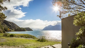 A coastal landscape with a clear sky, a body of water, and a wooden structure. - The Camp - Lake Hawea (Lake Hawea)