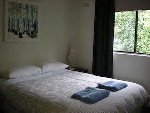 Relax in this serene retreat with a comfortable bed, a painting of a forest scene, and a window offering a view of lush greenery.