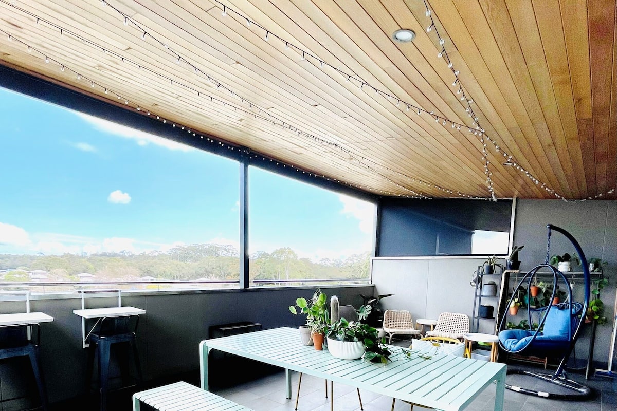 Ein modernes Interieur mit Holzboden, einem großen Fenster, einem Tisch mit Stühlen und Topfpflanzen.