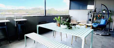 A modern interior with a wooden ceiling, a large window, a table with chairs, and potted plants.