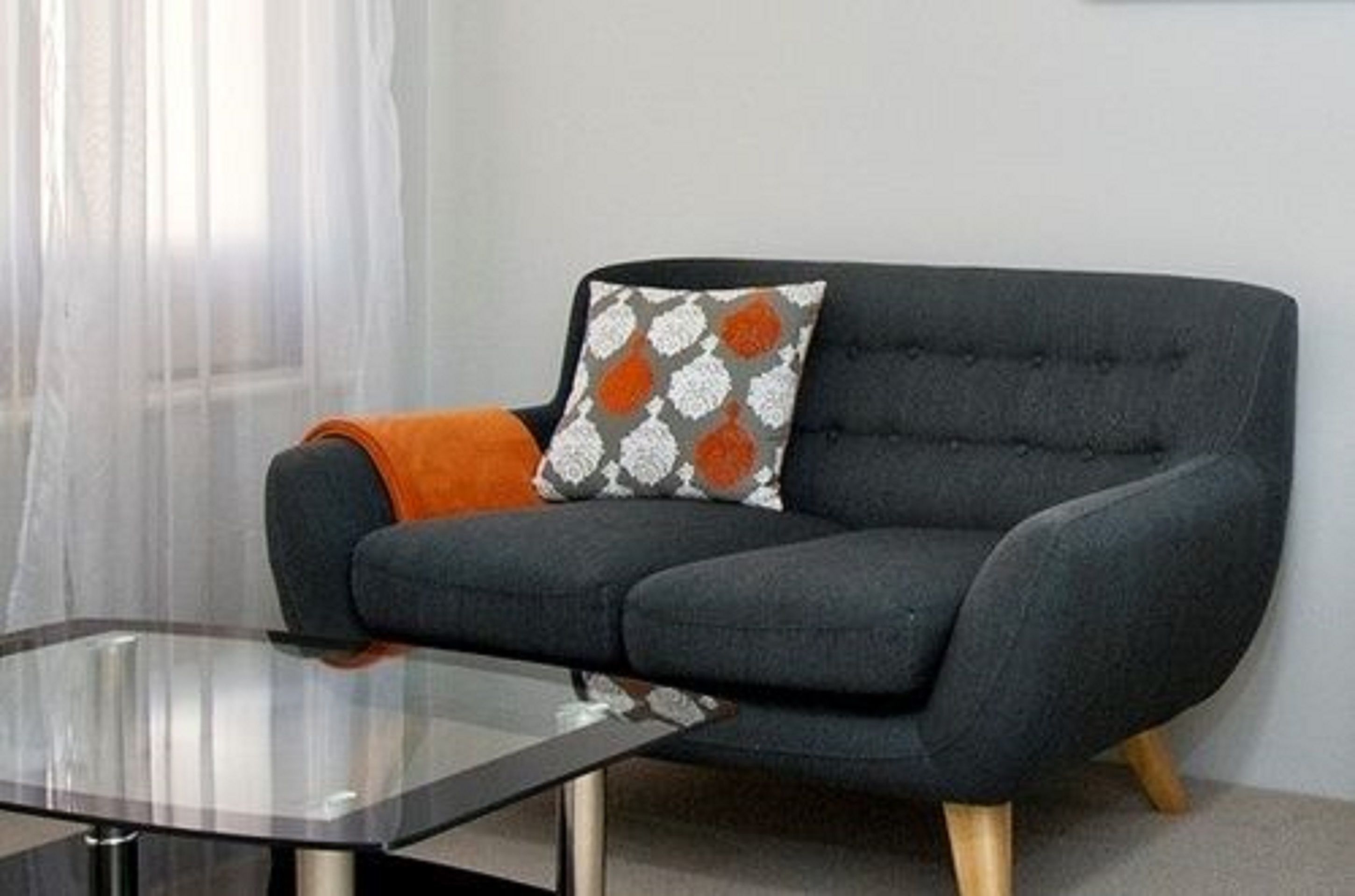 A modern living room with a dark grey sofa, a patterned throw pillow, and a glass coffee table.
