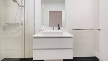 Un baño moderno con cabina de ducha de vidrio, tocador blanco con espejo y suelo de baldosas negras.