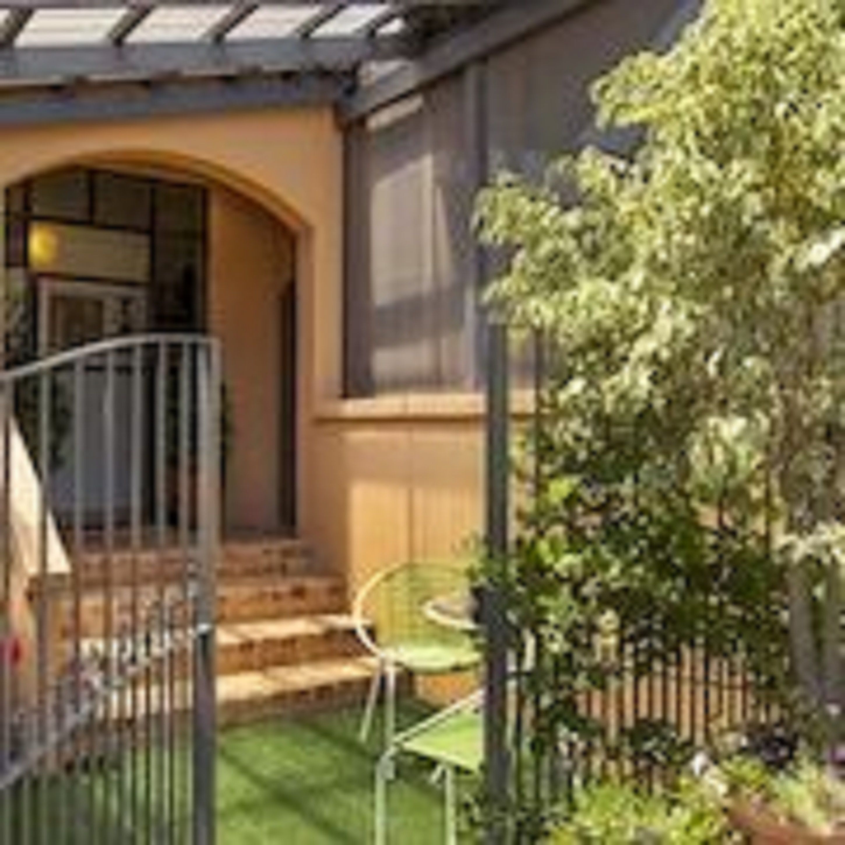 A covered patio with a curved railing, a small staircase leading to a door, and a green lawn area with a chair.