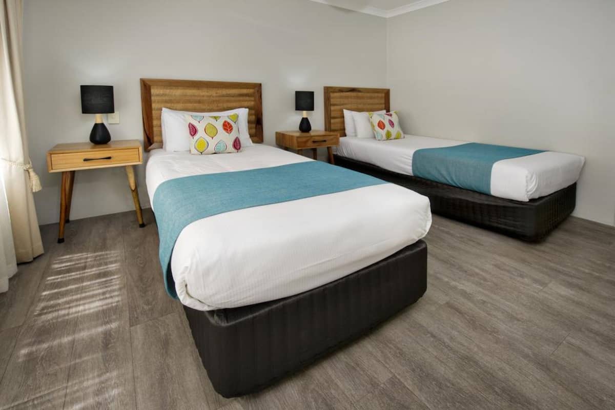 Ein Hotelzimmer mit zwei Betten, Holz-Kopfteilen und einer blauen Decke.