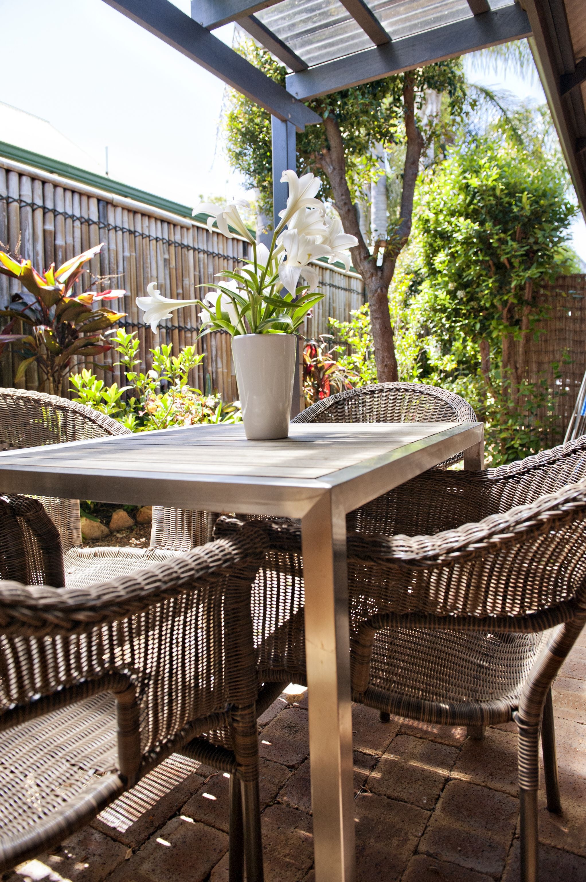 Un patio techado con mobiliario de mimbre, una mesa y una planta en maceta.