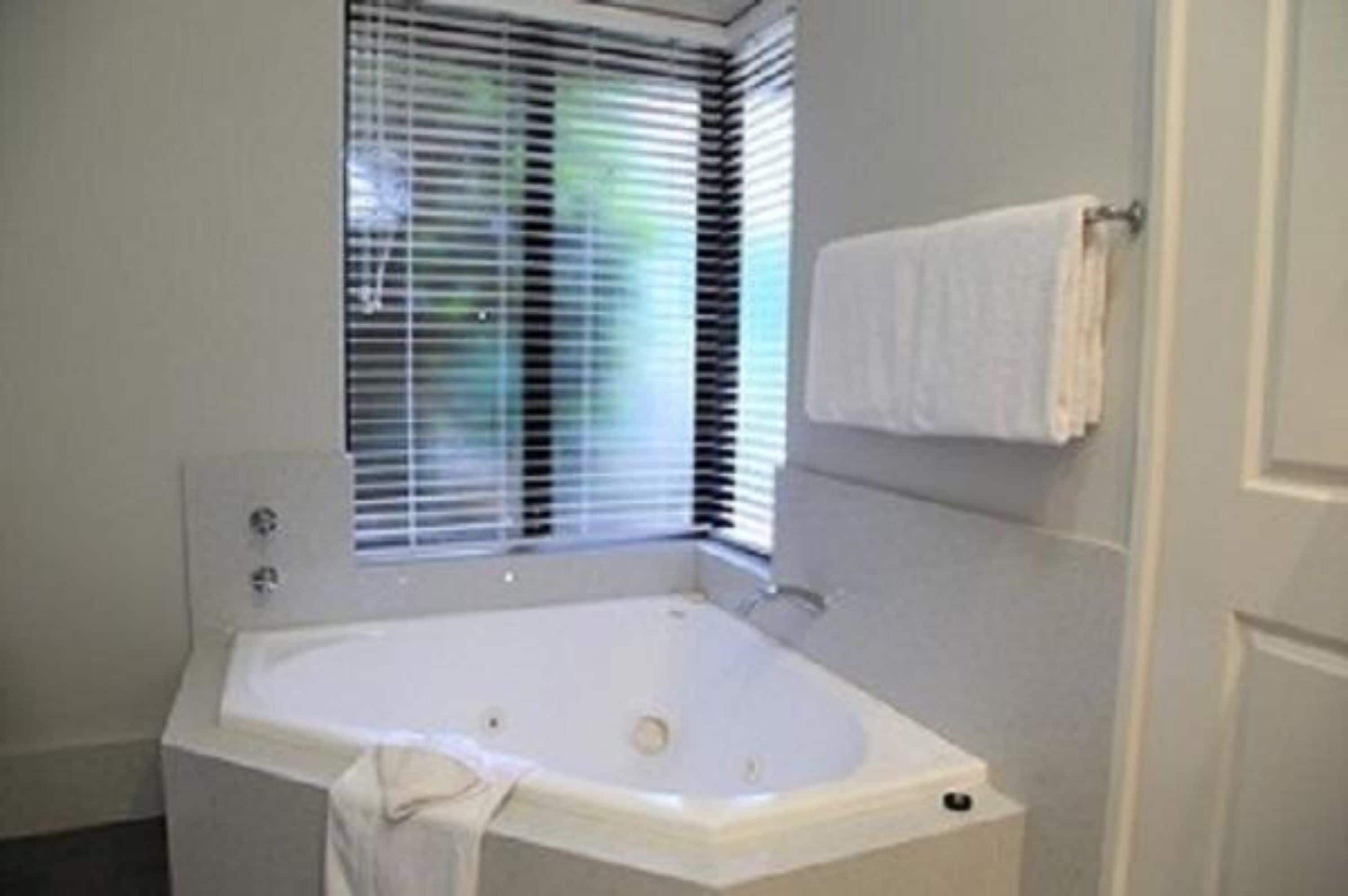 Une salle de bain avec une baignoire, une fenêtre avec des stores et un porte-serviettes.