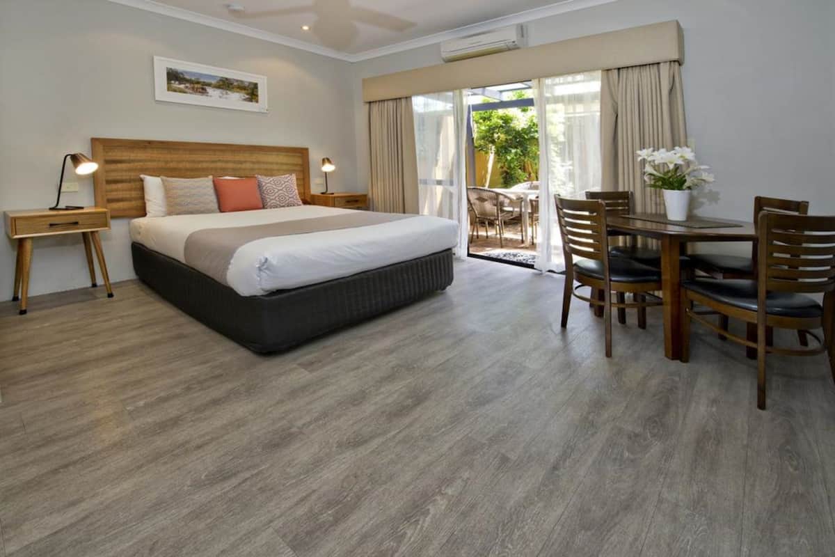 Ein Hotelzimmer mit einem großen Bett, einem Esstisch mit Stühlen, einem kleinen Beistelltisch und Blick ins Freie durch eine Schiebetür.