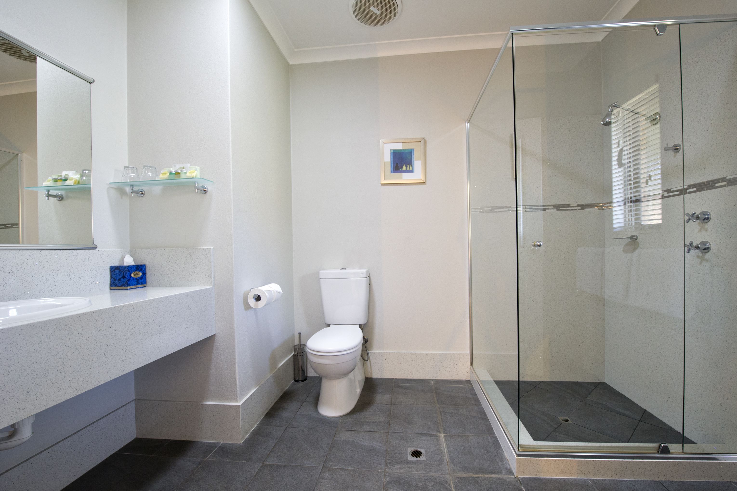 Un baño con inodoro, cabina de ducha de vidrio y lavabo con espejo.