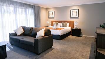 A modern hotel room with a grey sofa, a double bed, and a nightstand with a lamp.