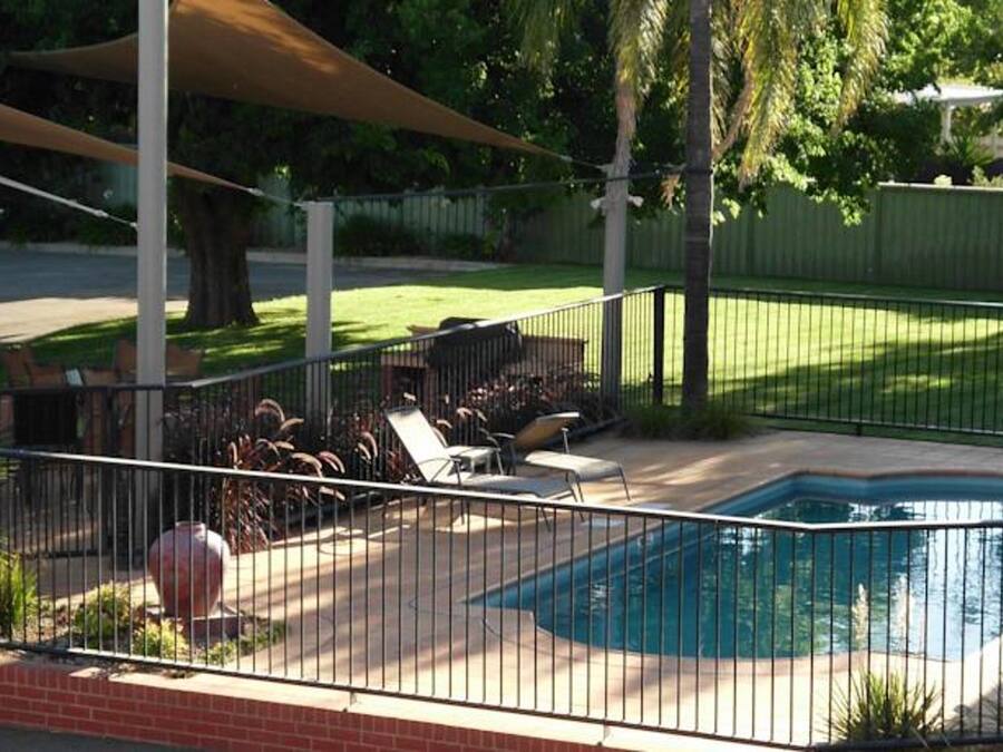 Patio trasero con piscina, terraza techada y zona vallada con sillones de descanso.
