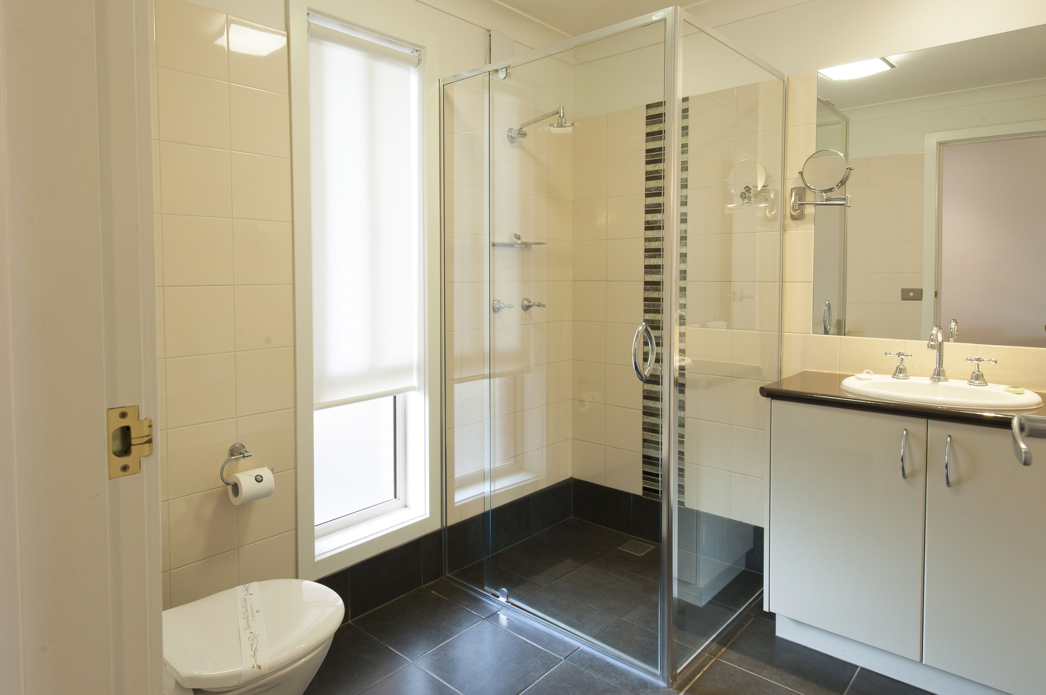 Un baño moderno con ducha de vidrio, inodoro y tocador con lavamanos.