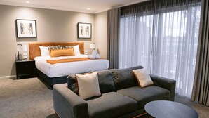 A hotel room with a bed, a sofa, a small table, and a large window with curtains. - Rsl Club Motel (Wagga Wagga)