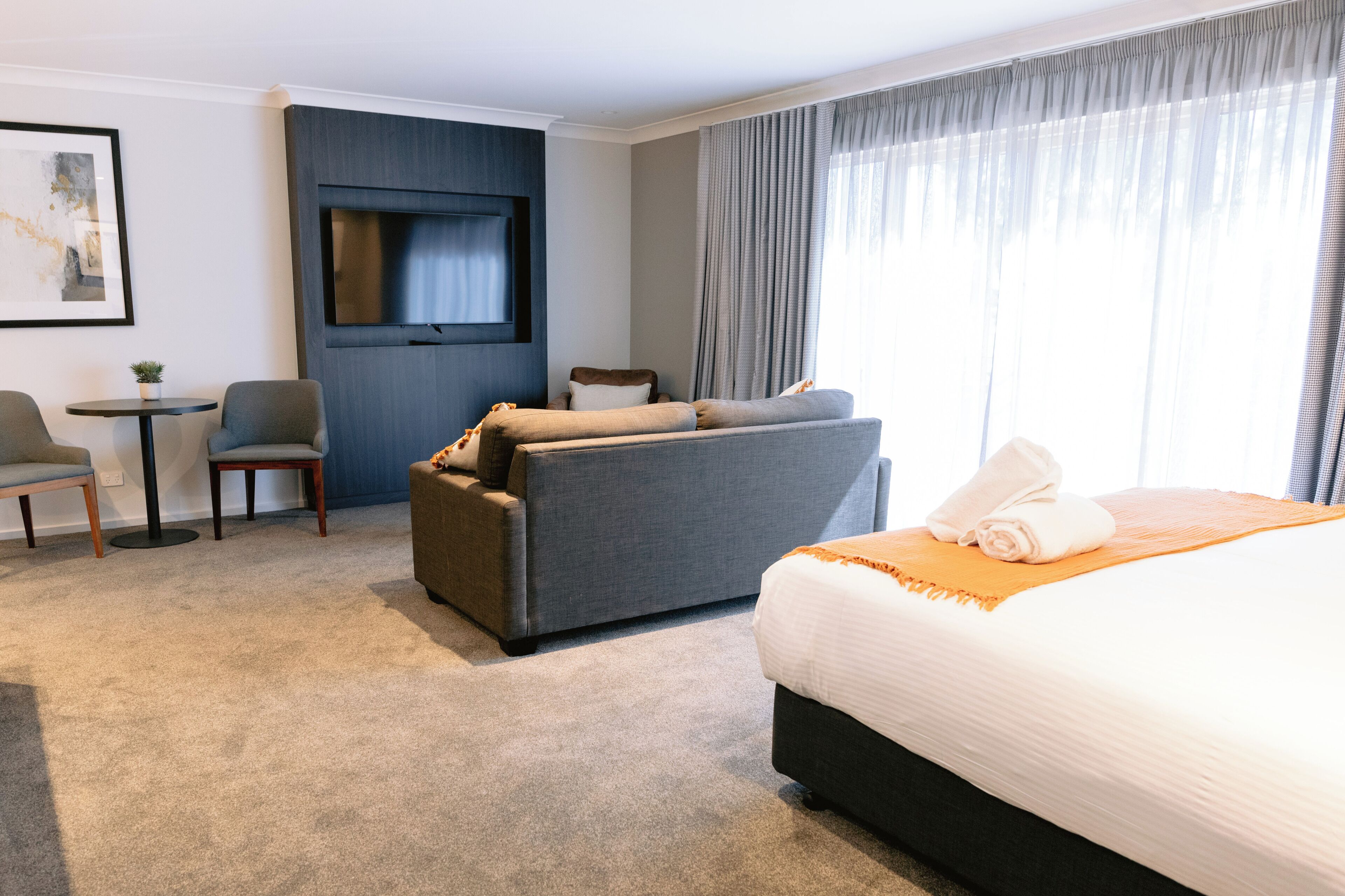 Une chambre d’hôtel avec un grand lit, un canapé, un téléviseur fixé au mur et une petite table avec une chaise.